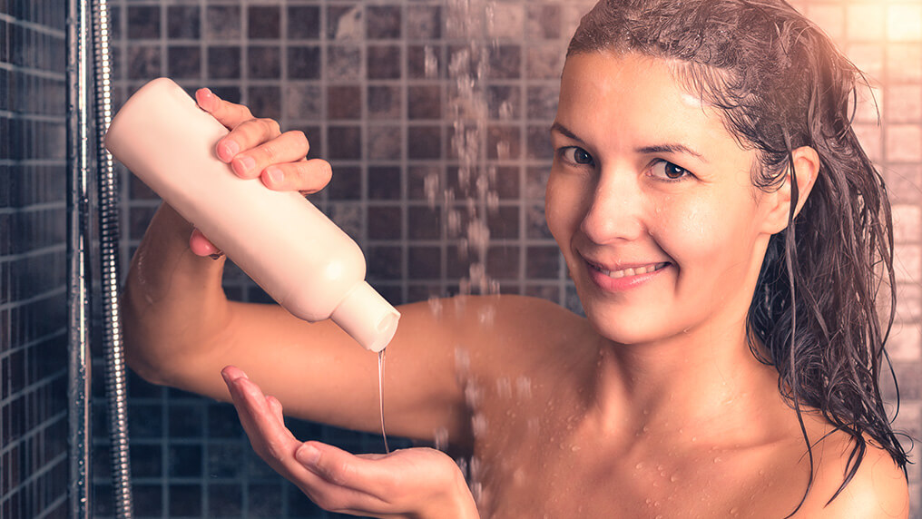 Mulher tomando banho, de frente, sorrindo, colocando o shampoo na mão fazendo low poo