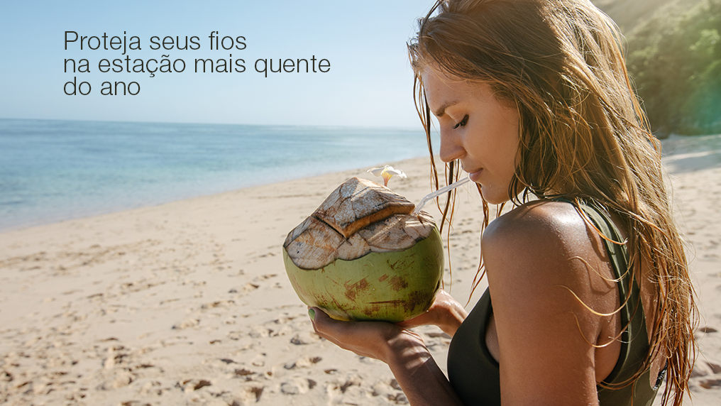 Mulher na praia bebendo água de coco no verão
