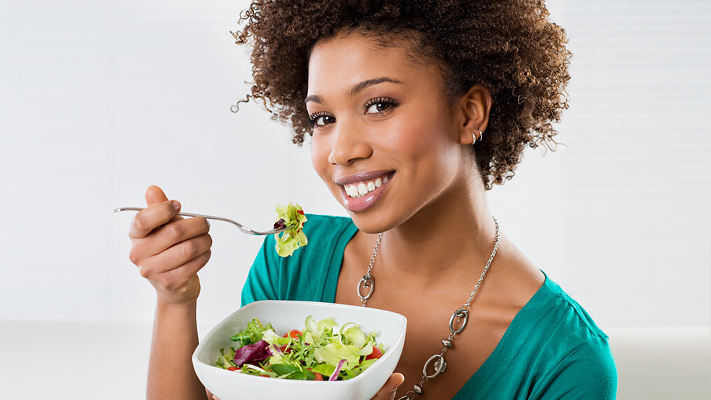 Mulher morena comendo salada para evitar o enfraquecimento dos fios.